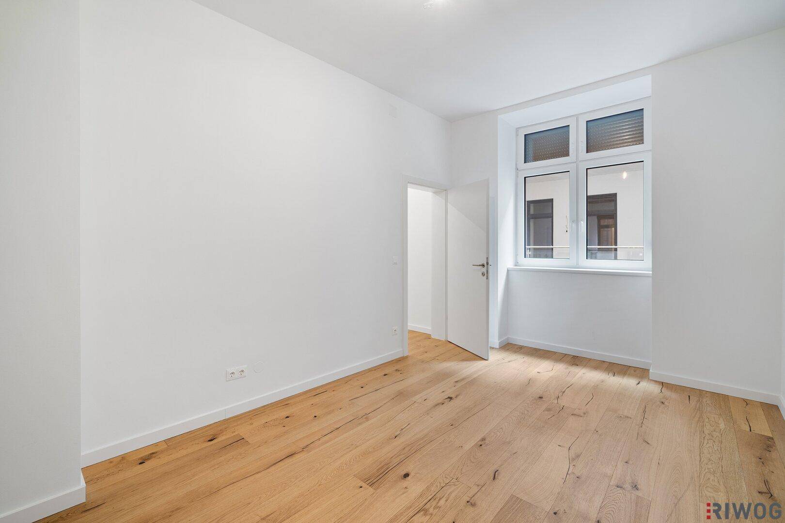 Helles Schlafzimmer mit Holzboden und großem Fenster, bereit zur individuellen Gestaltung.
