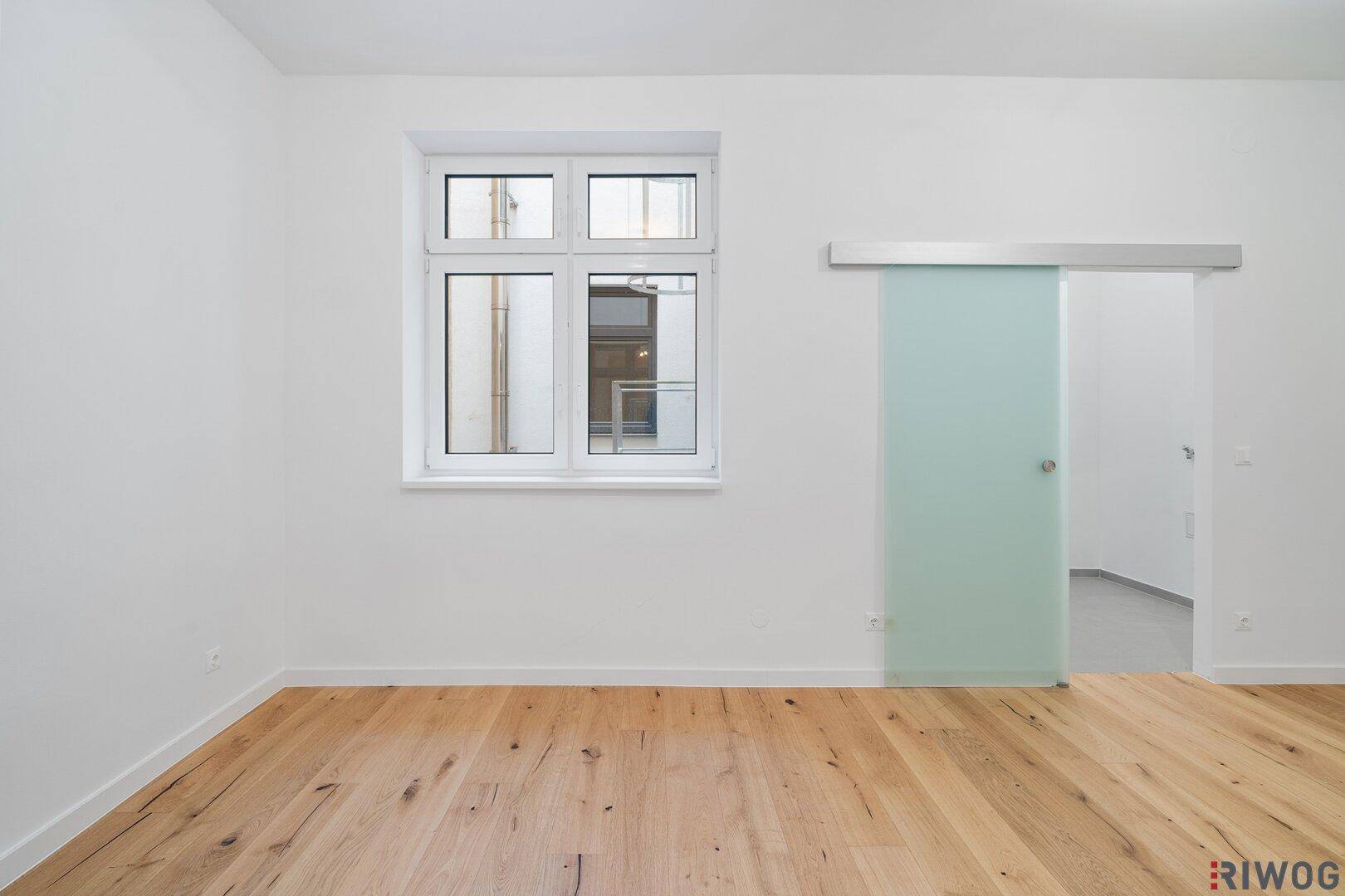 Lichtdurchfluteter Raum mit großem Fenster und einer eleganten Glasschiebetür.