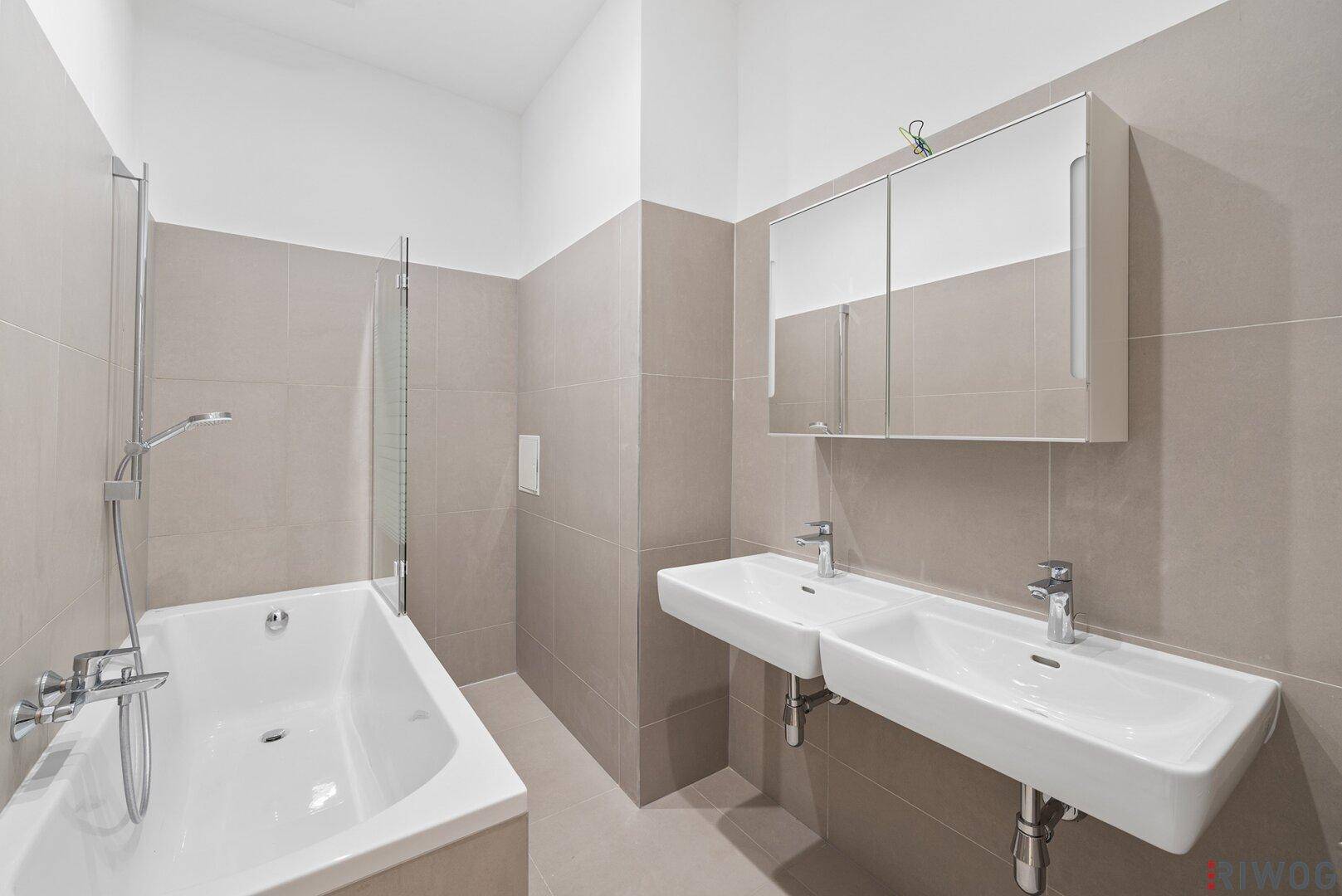 Modernes Badezimmer mit Doppelwaschbecken, Badewanne und hellen Fliesen.