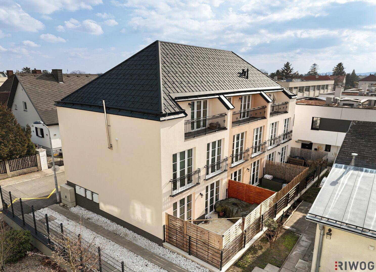 Luftaufnahme der Gebäudeseite mit kleinen privaten Gartenbereichen, Holzzäunen und moderner Architektur.