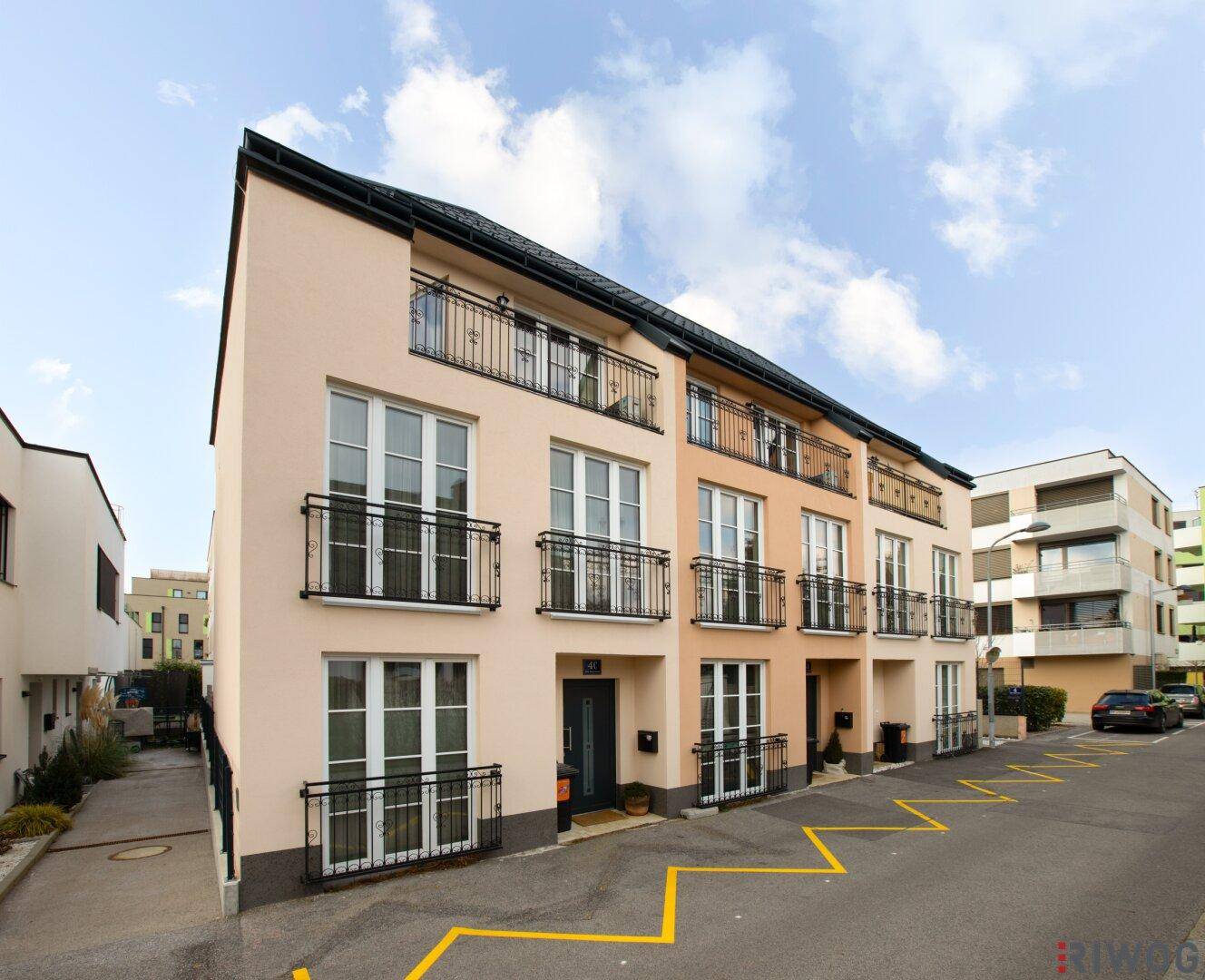 Seitenansicht des modernen Wohngebäudes mit hellbeiger Fassade, französischen Balkonen und klaren Linien.