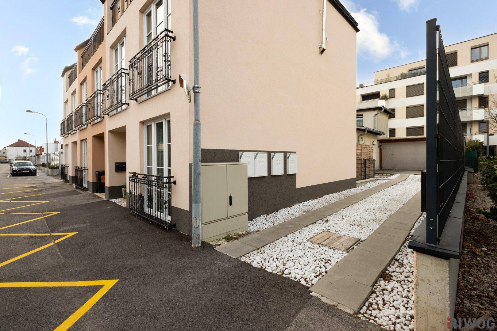 Seitenansicht des Gebäudes mit Zufahrt, Kiesstreifen und einem modernen, gepflegten Außenbereich.