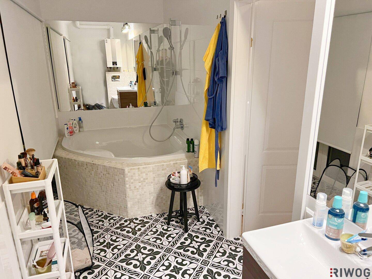 Modernes Badezimmer mit Eckbadewanne, Duschbereich und auffälligen, gemusterten Bodenfliesen.