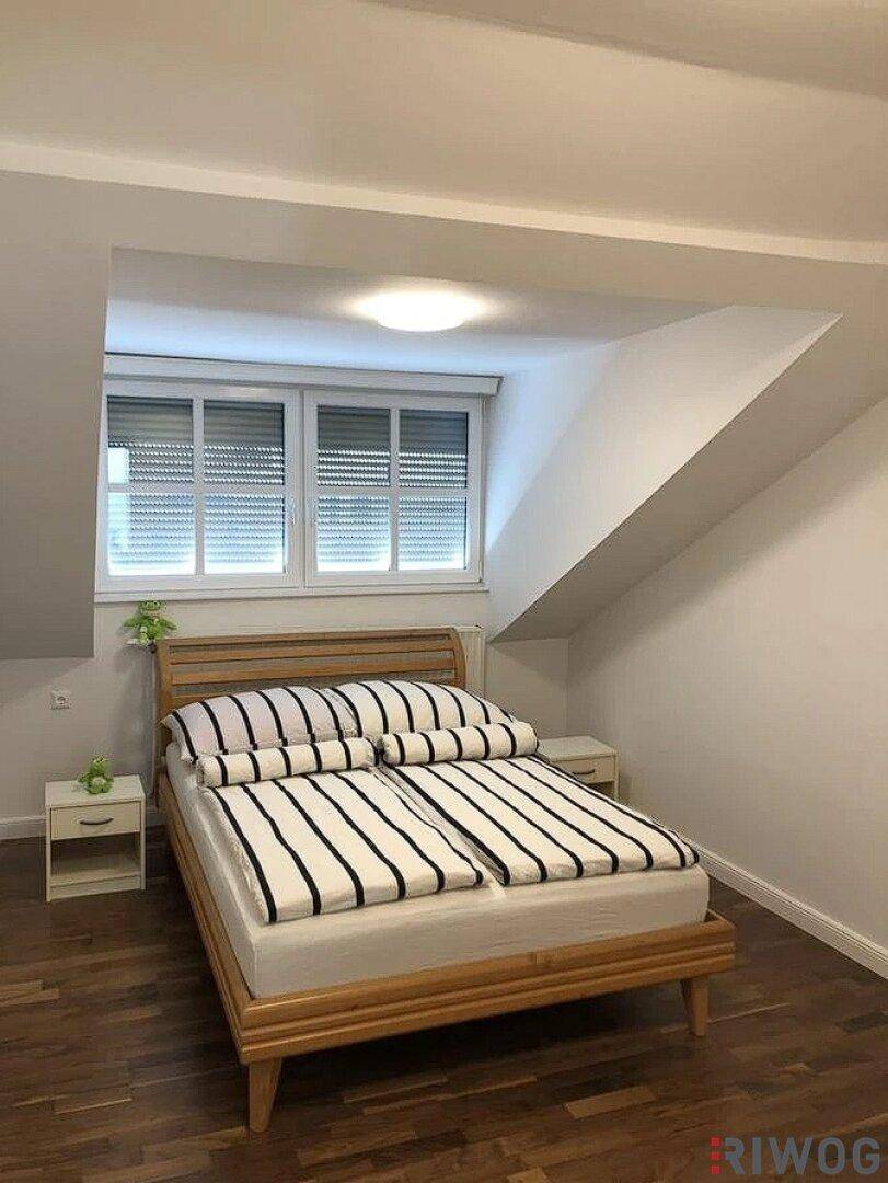 Gemütliches Schlafzimmer mit Holzbett, Parkettboden und Dachschräge unter dem Fenster, hell und einladend.