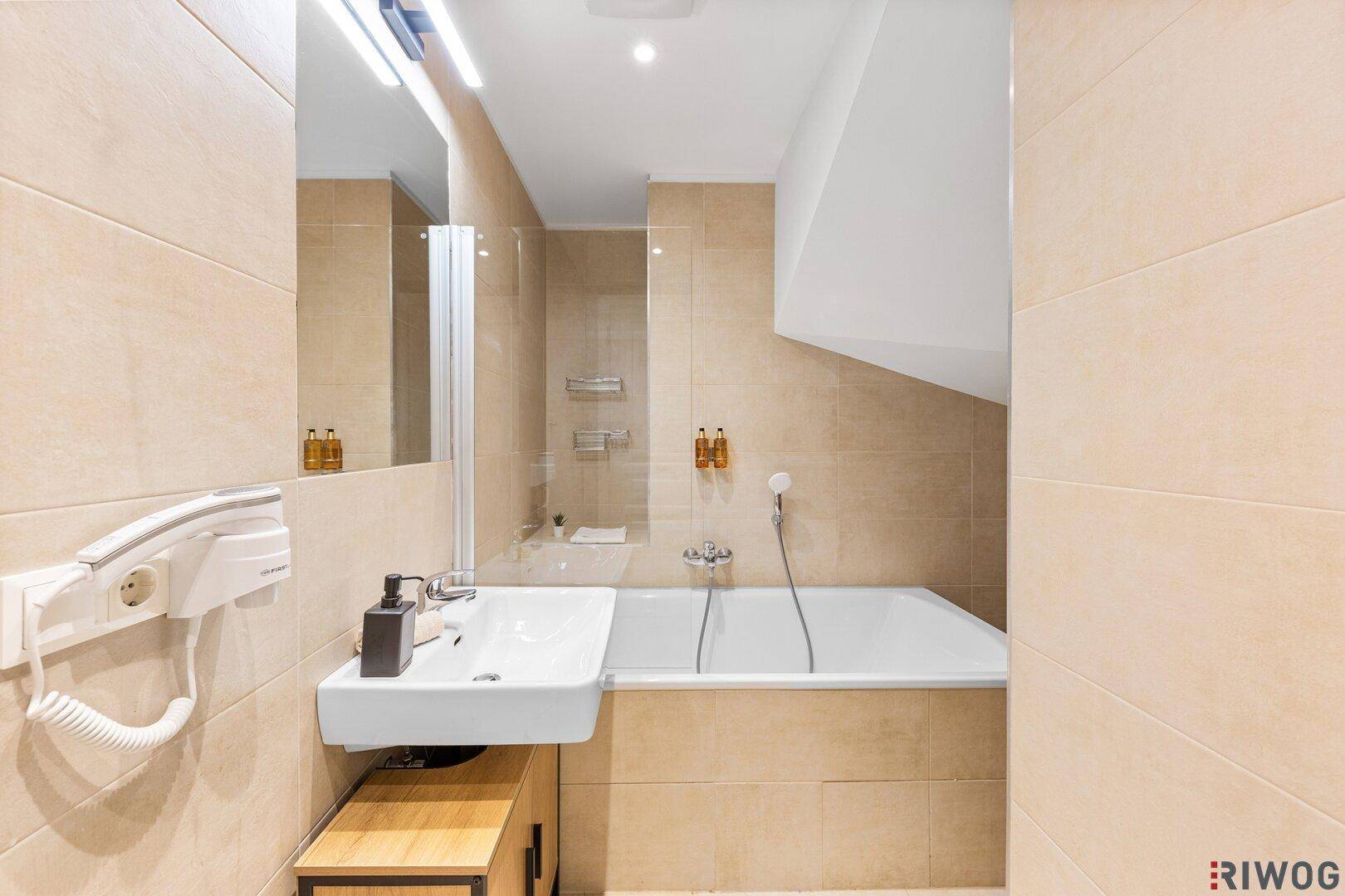 Modernes Badezimmer mit Badewanne, Waschbecken und beigefarbenen Wandfliesen.