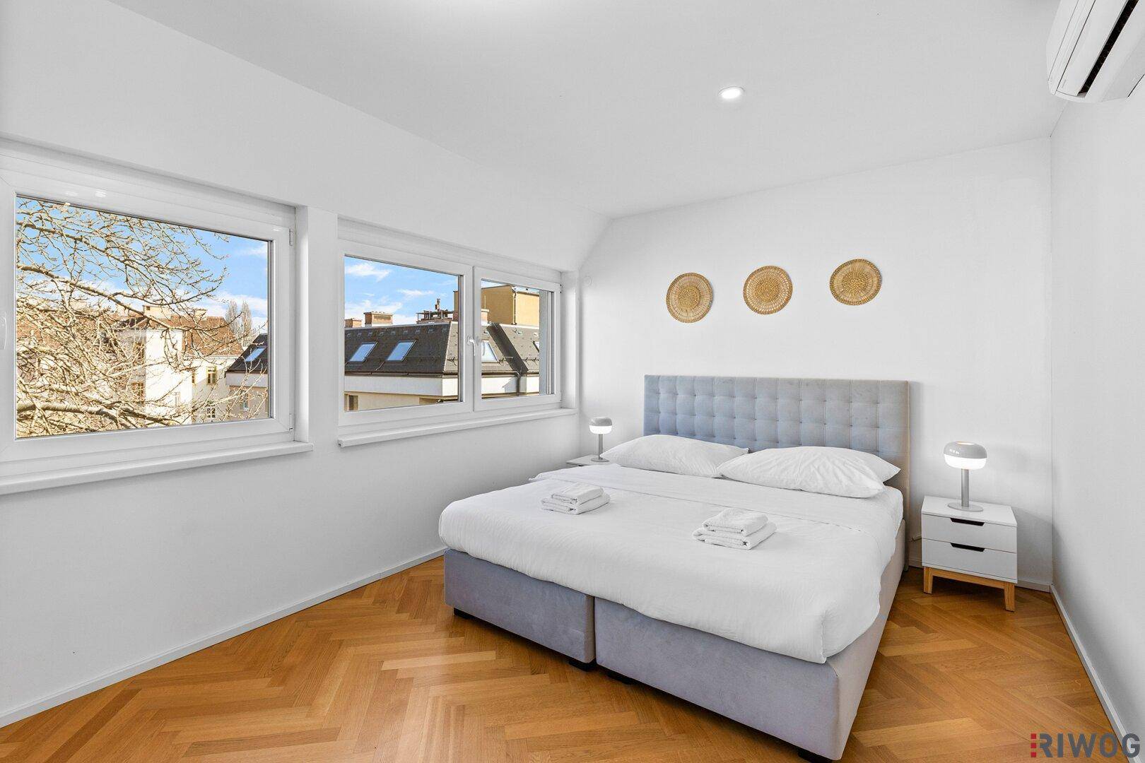 Gemütliches Schlafzimmer mit Parkettboden, großen Fenstern und Blick ins Grüne.