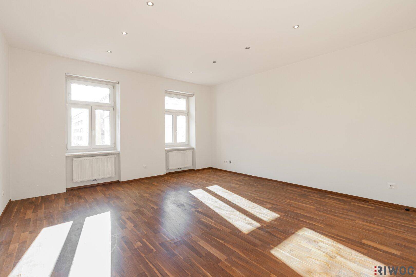 Geräumiger Wohnbereich mit Parkettboden und viel Tageslicht durch die Fenster.