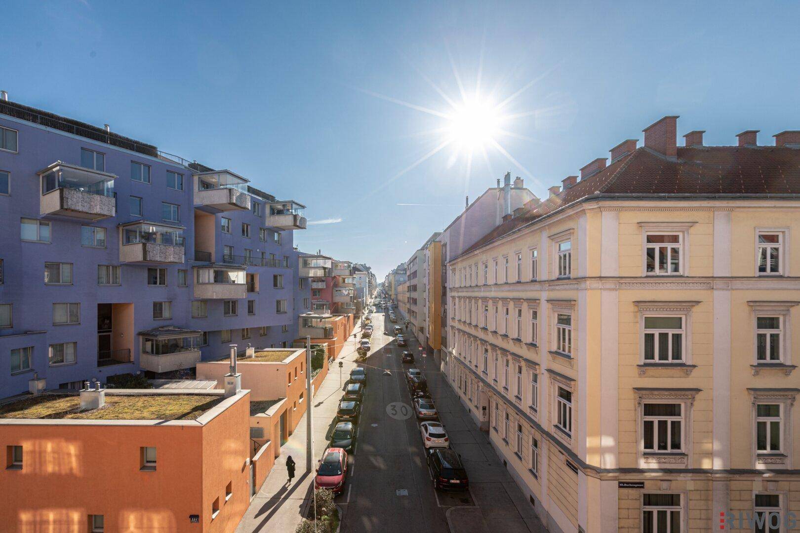 Blick von oben auf eine belebte Stadtstraße mit verschiedenen Wohngebäuden unter blauem Himmel.