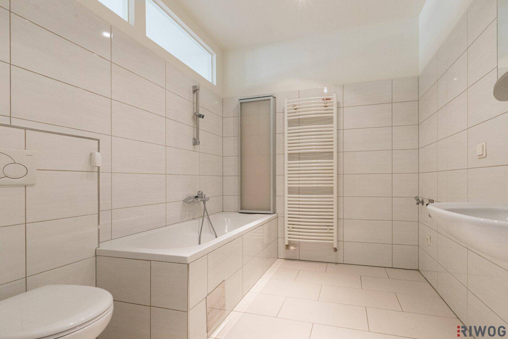 Helles Badezimmer mit Badewanne, WC, Waschbecken und weißen Wand- und Bodenfliesen.