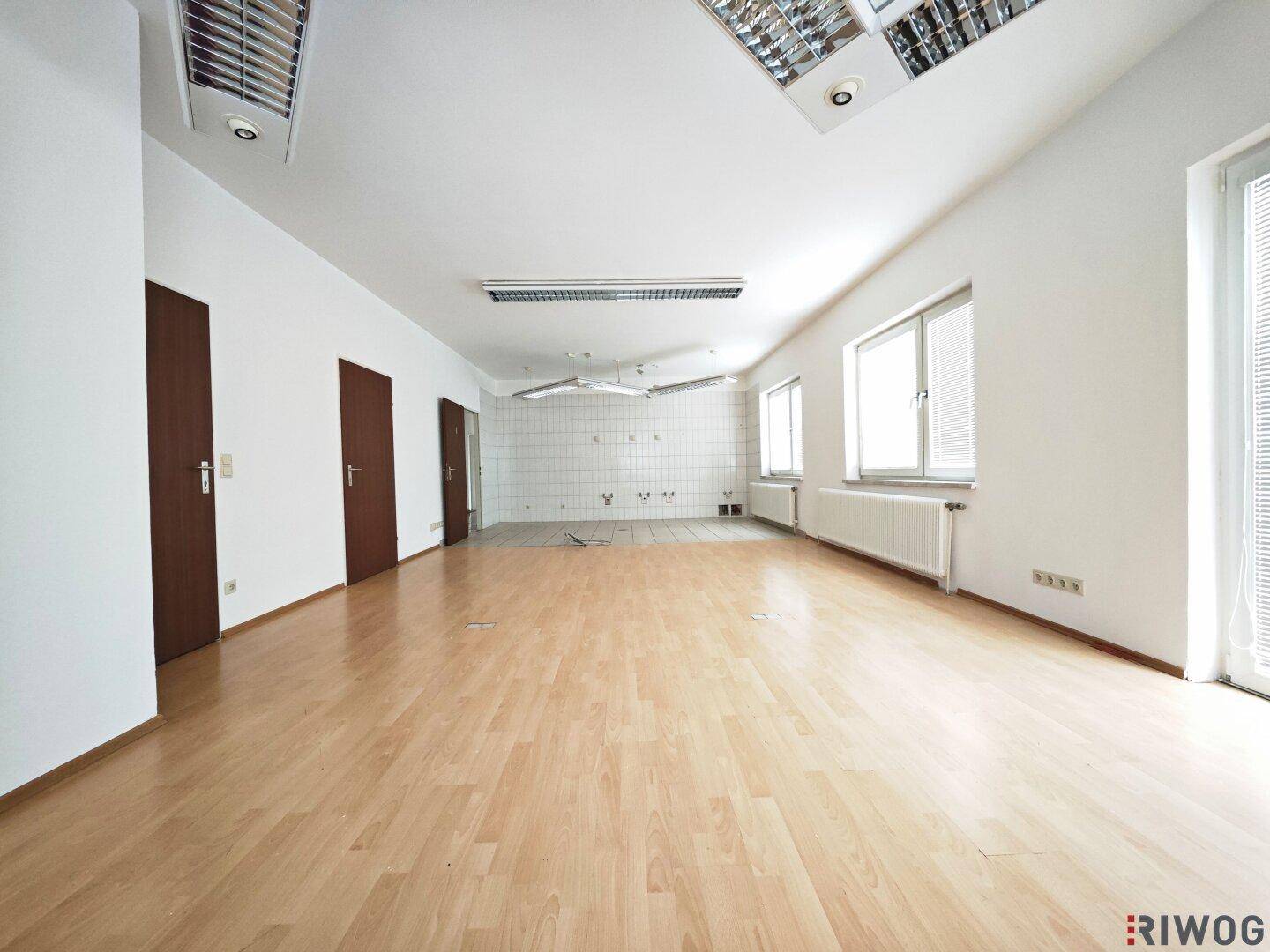 Heller Büroraum mit Laminatboden, weißen Wänden und mehreren Fenstern, bietet viel Tageslicht.