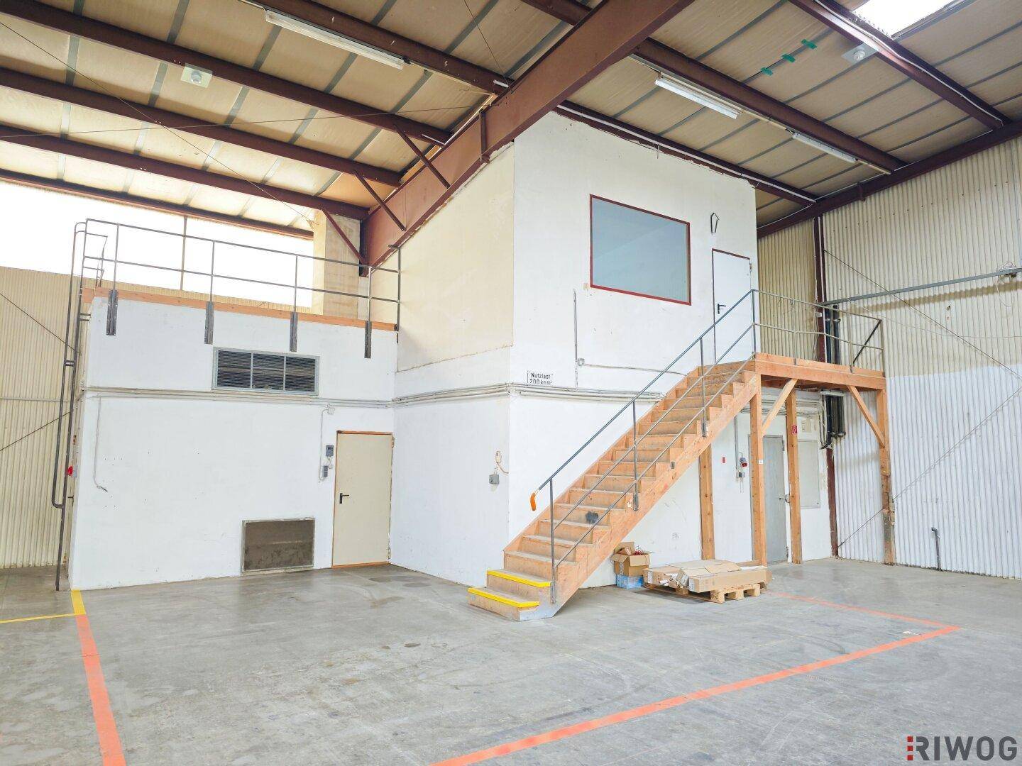 Mehrstöckiger Bürobereich innerhalb einer Lagerhalle mit Holztreppe und Geländer.