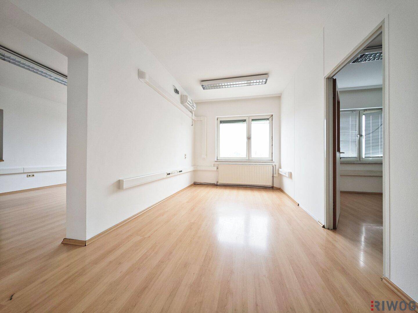 Geräumiger Büroraum mit Laminatboden, weißen Wänden und einem Fenster, das viel Tageslicht bietet.