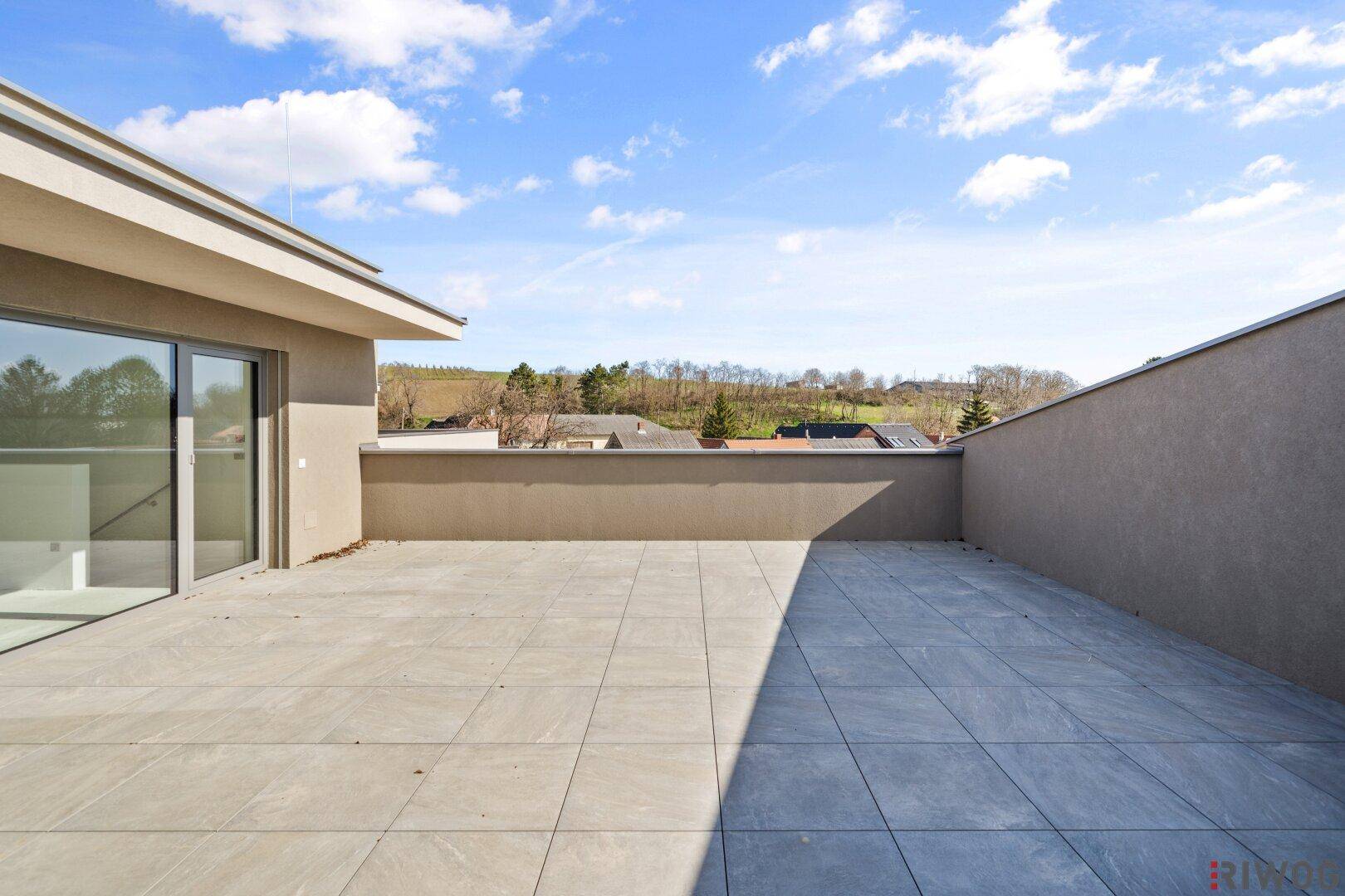 Sonnige Dachterrasse mit Fliesenboden und weitem Blick auf die Landschaft und den Himmel.