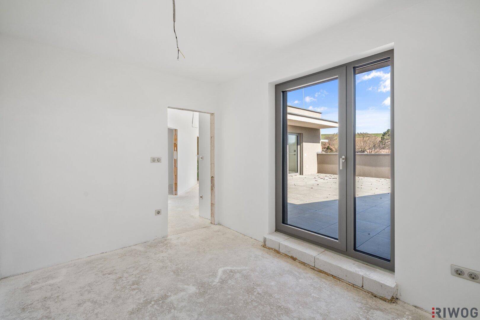 Unfertiges Zimmer mit Terrassenzugang und Rohbetonboden, bereit für den Innenausbau.