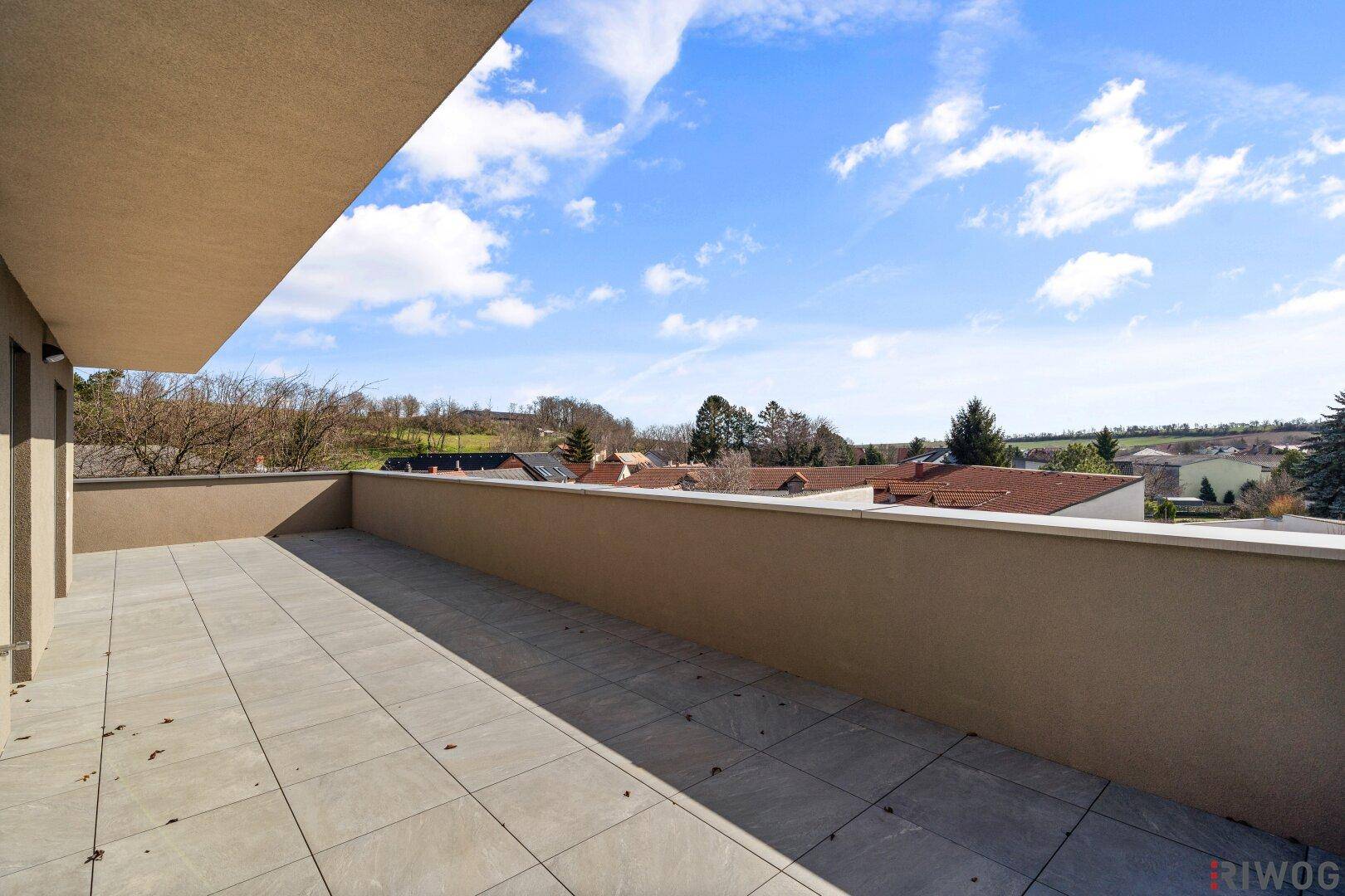 Geräumige Dachterrasse mit Fliesenboden und weitem Blick über die Landschaft unter blauem Himmel.