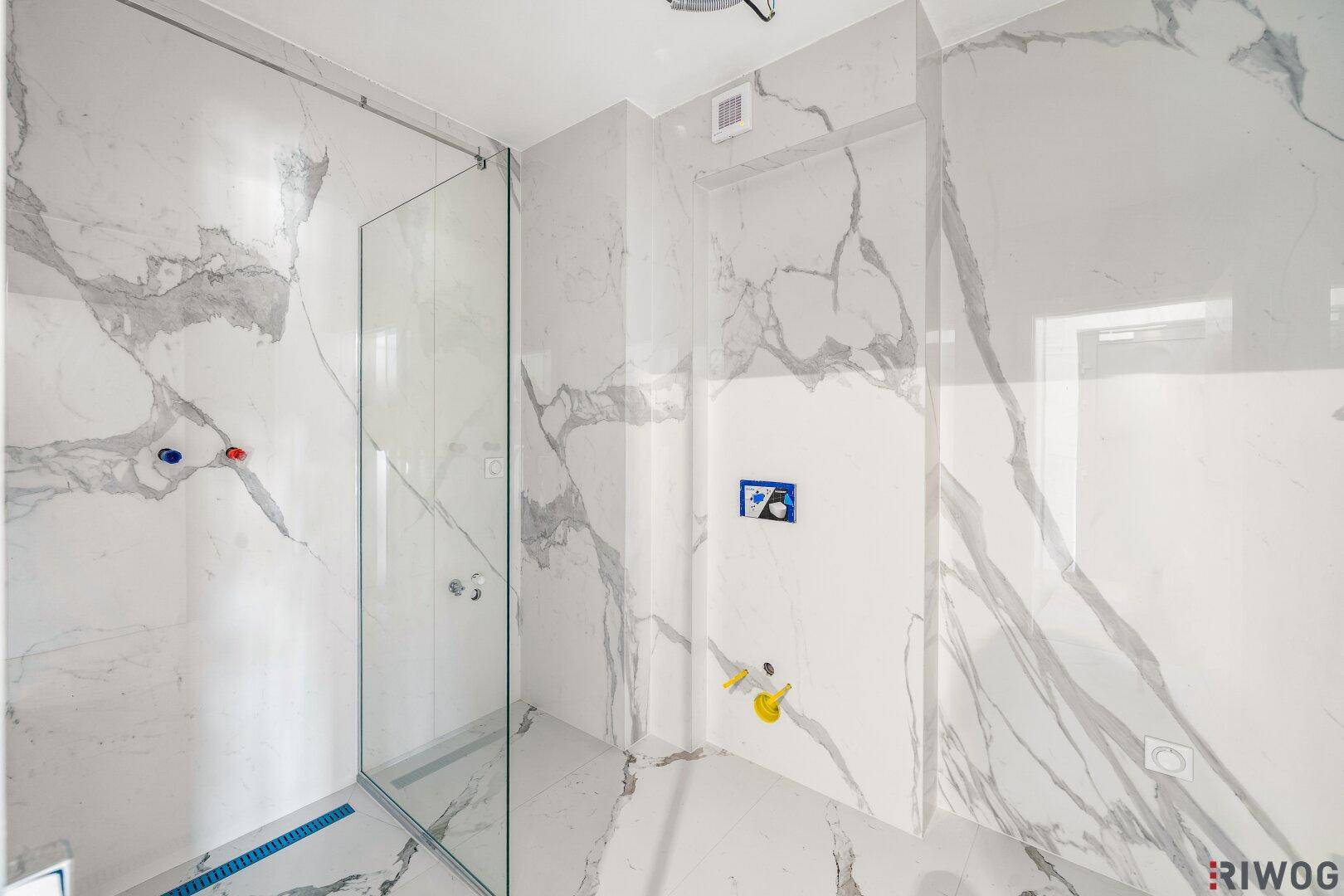 Unfertiges Badezimmer mit Marmorfliesen, vorbereiteten Anschlüssen für Dusche und Toilette.