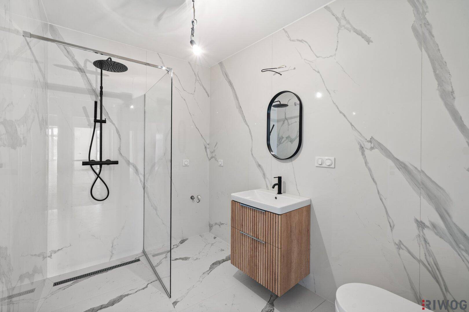 Modernes Badezimmer mit großformatigen Marmorfliesen, ebenerdiger Dusche und elegantem Waschtisch.