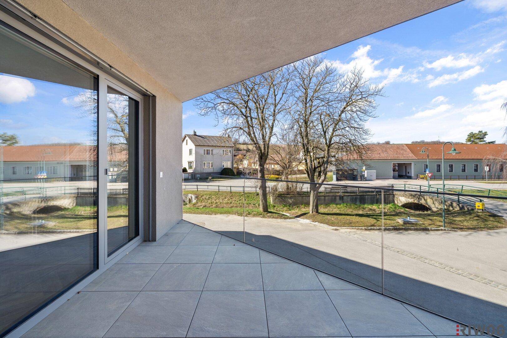 Heller Balkon mit Fliesenboden und Glasgeländer, bietet einen weiten Blick auf die ländliche Umgebung.
