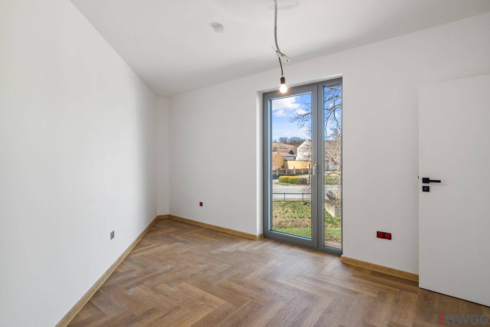 Lichtdurchflutetes Zimmer mit Fischgrätparkett und großem Fenster mit Blick ins Grüne.