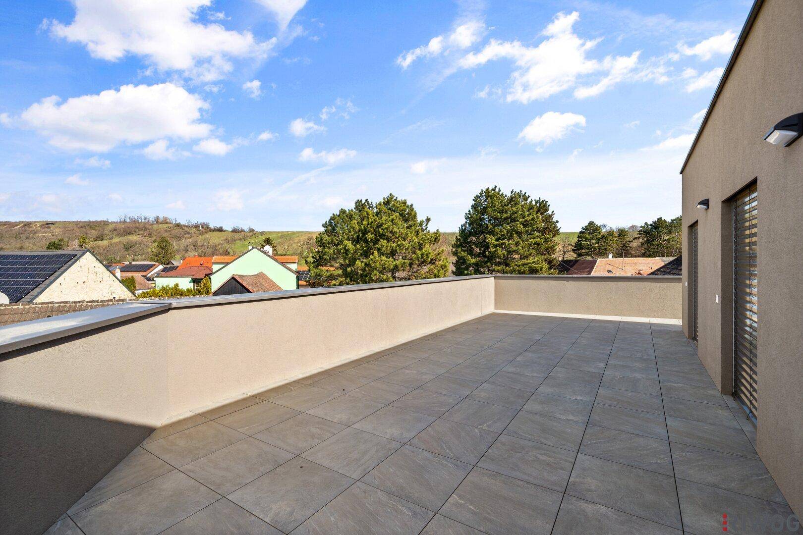 Sonnige Dachterrasse mit Fliesenboden und unverbautem Blick auf die grüne Landschaft.