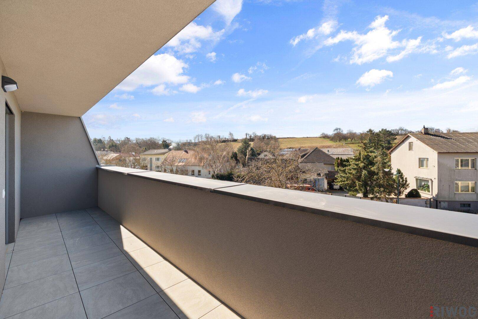 Langer Balkon mit Fliesenboden und solider Brüstung, bietet einen weiten Blick über die Nachbarschaft.