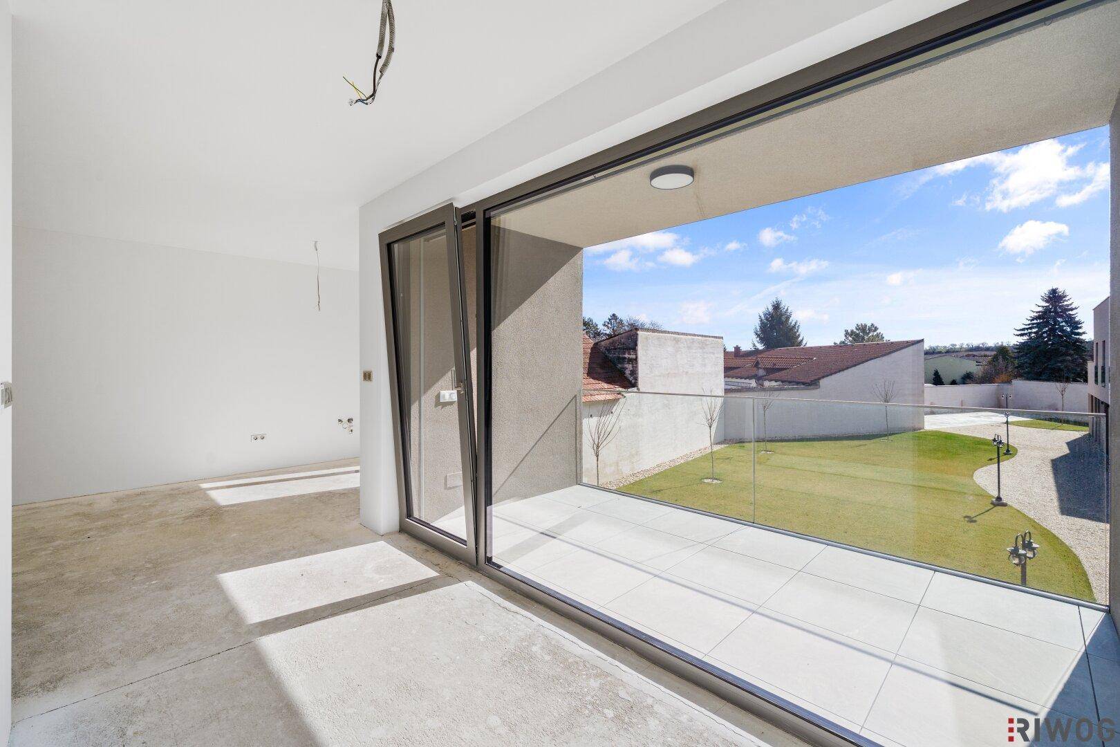 Unfertiger Wohnraum mit Betonboden und großen Schiebetüren zu einer gefliesten Terrasse.