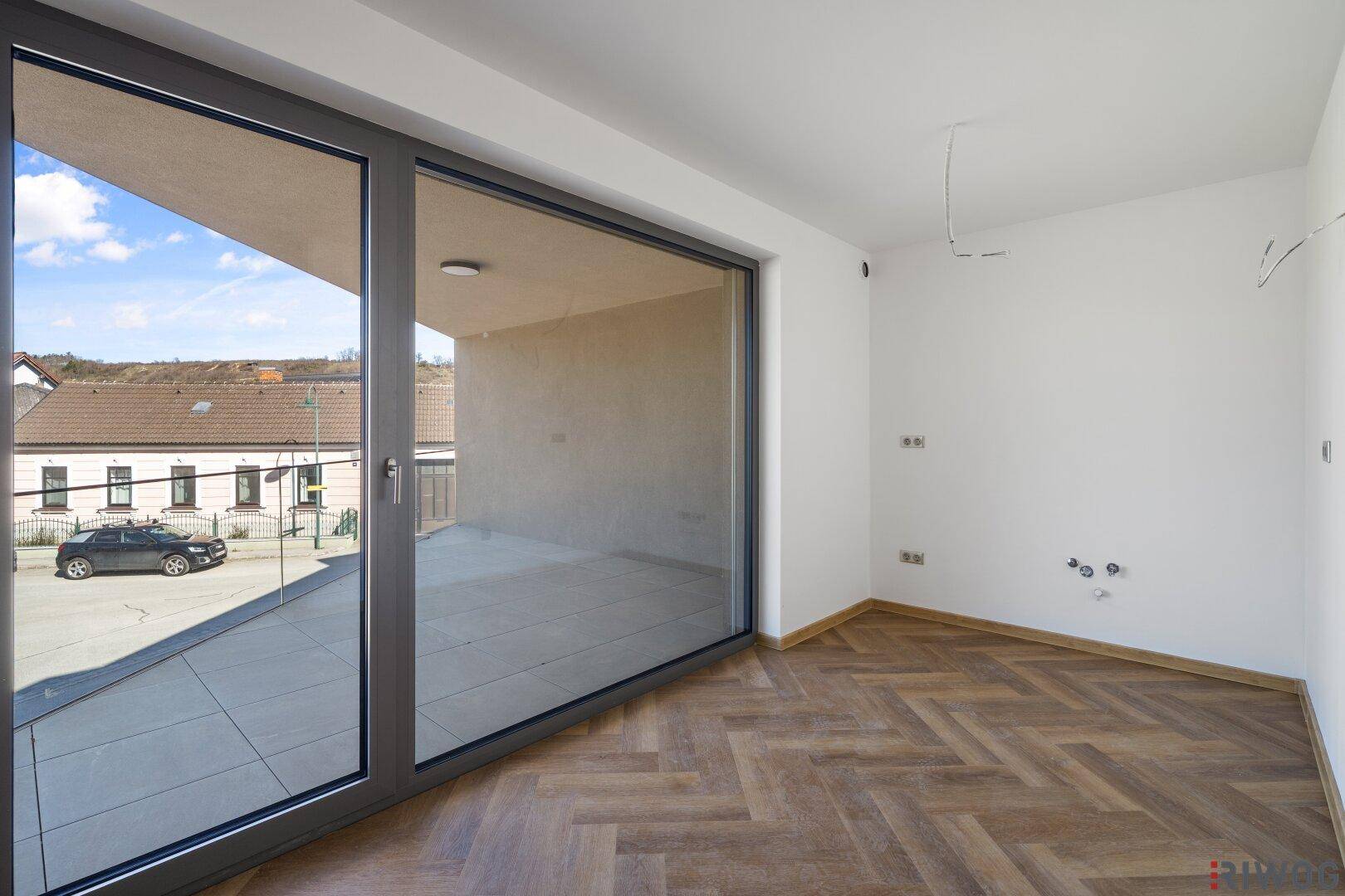 Wohnraum mit Fischgrätparkett und großer Glasfront, die den Außenbereich widerspiegelt.