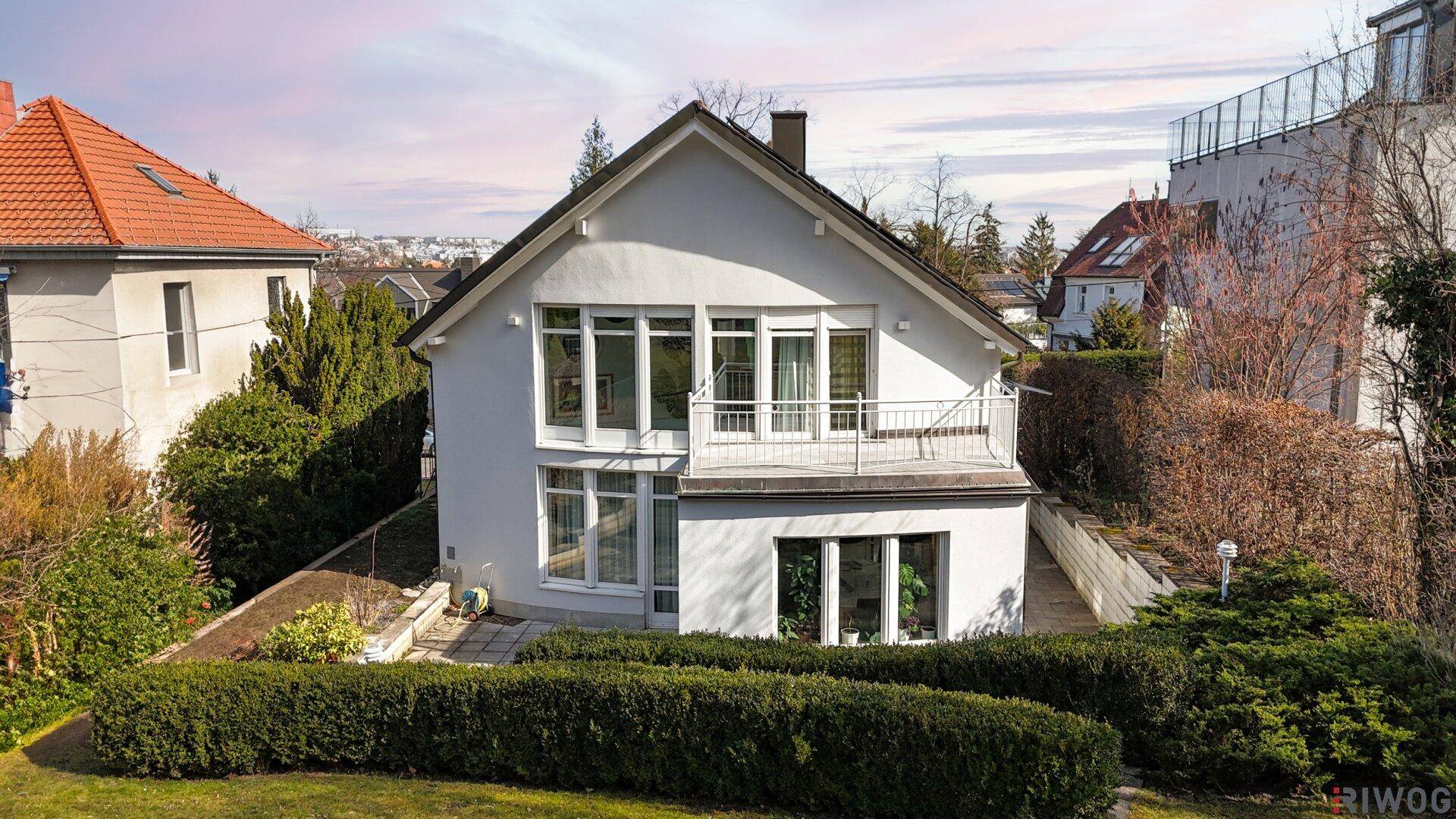 Rückansicht des Hauses mit gepflegtem Garten, Hecken und einer Terrasse im Erdgeschoss.