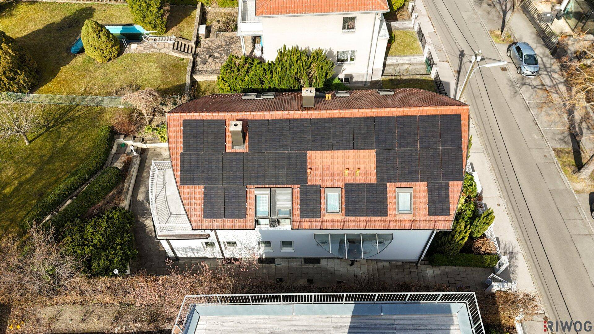 Draufsicht auf das Haus mit Solarpaneelen auf dem Ziegeldach und angrenzender Straße.