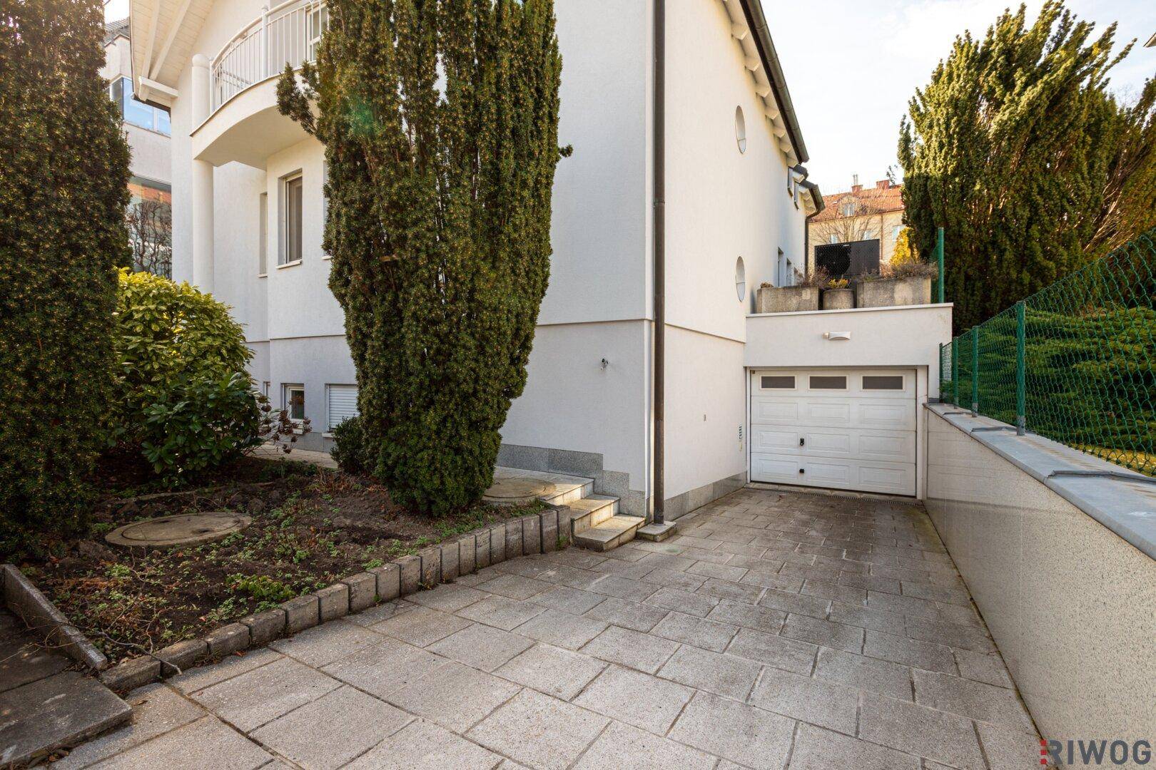 Garagenzufahrt mit gepflastertem Bereich und weißem Garagentor.