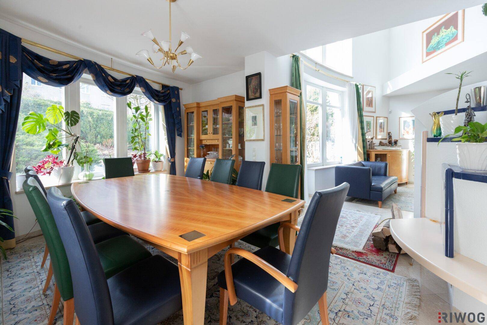 Eleganter Essbereich mit großem Holztisch, blauen Vorhängen und Blick in den Garten.