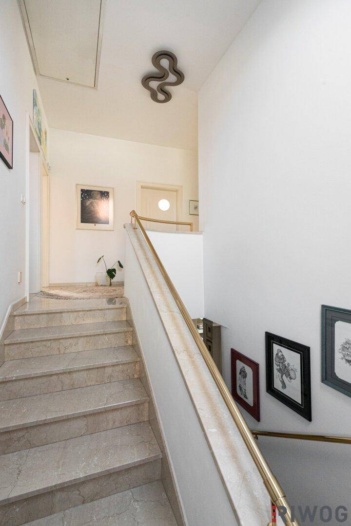 Geschwungene Treppe mit Marmorstufen und goldenem Handlauf führt ins Obergeschoss.