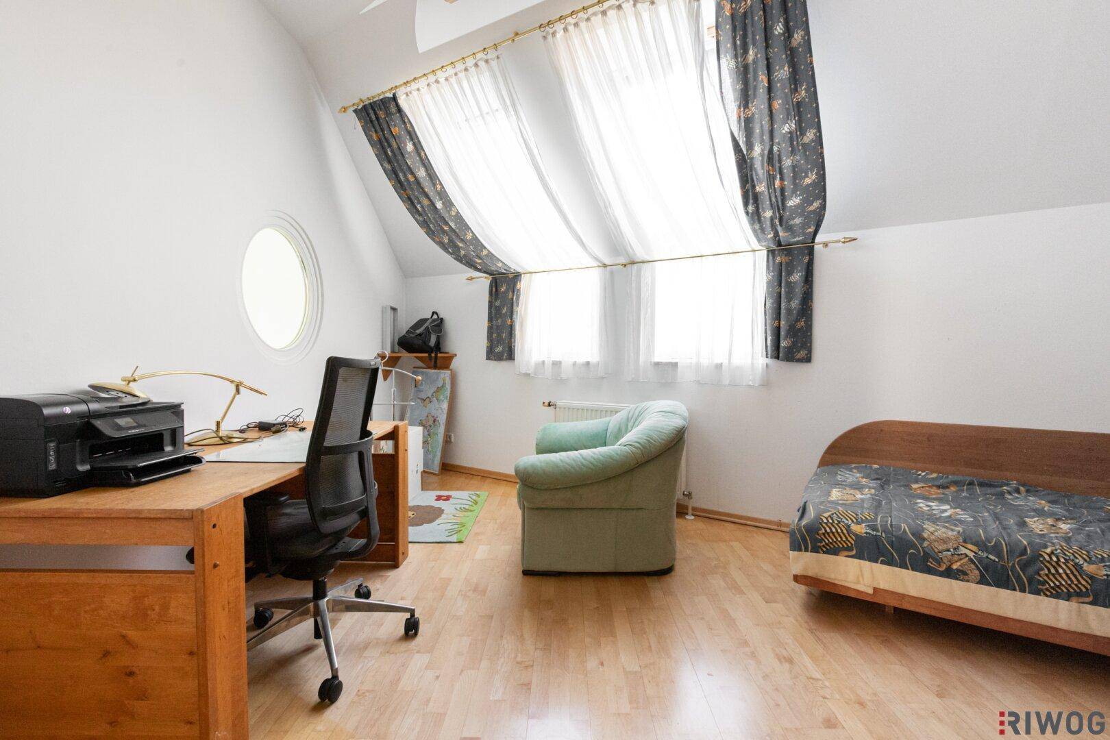 Zimmer im Dachgeschoss mit Holzboden, Schreibtisch und runden Fenstern.