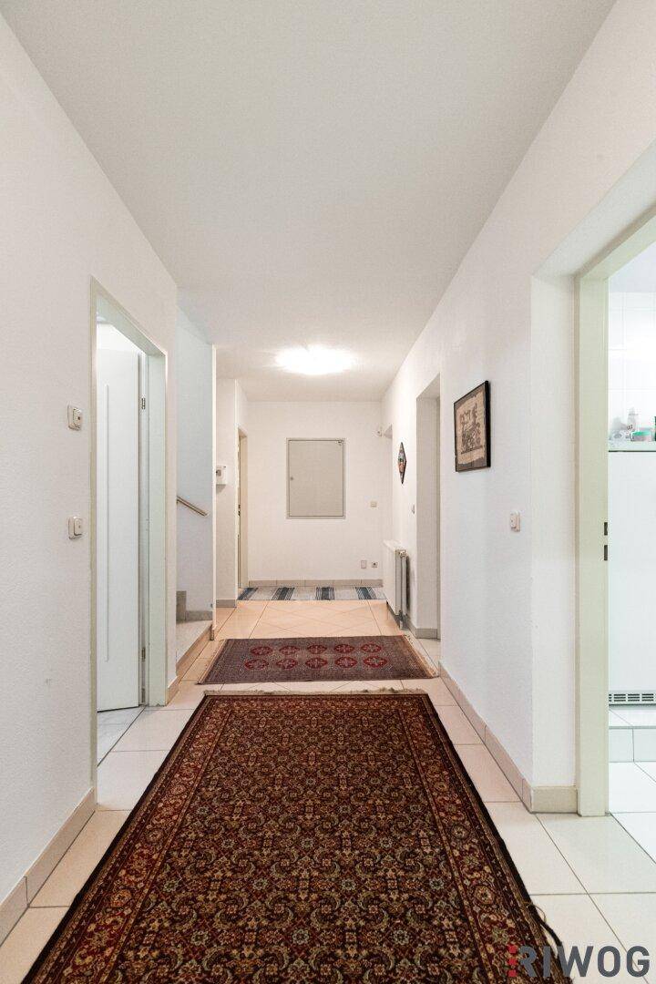 Langer Flur mit Fliesenboden und Teppichläufern, der zu den verschiedenen Räumen führt.