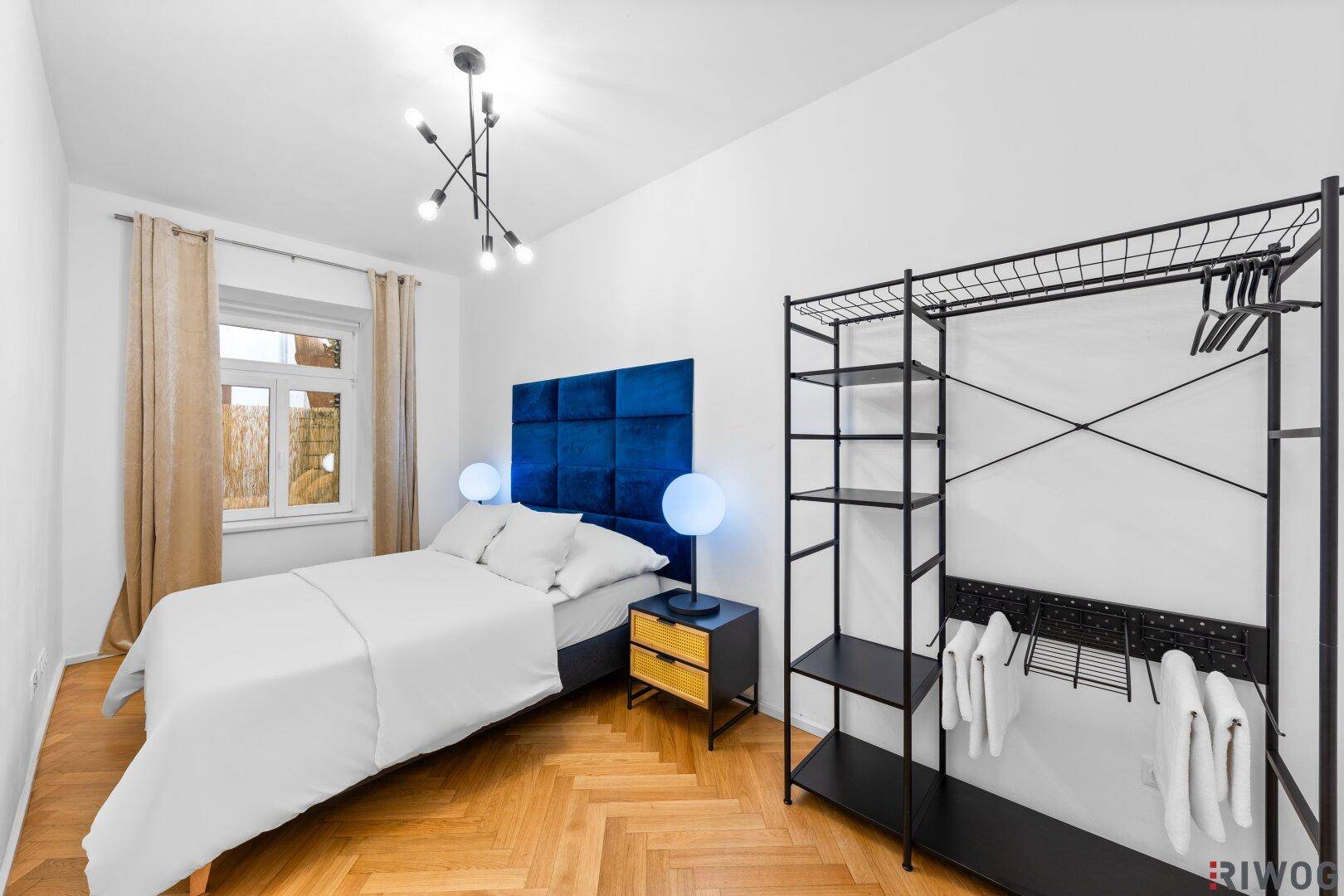 Schlafzimmer mit Doppelbett, modernem Kopfteil und offenem Kleiderschrank für zusätzlichen Stauraum.