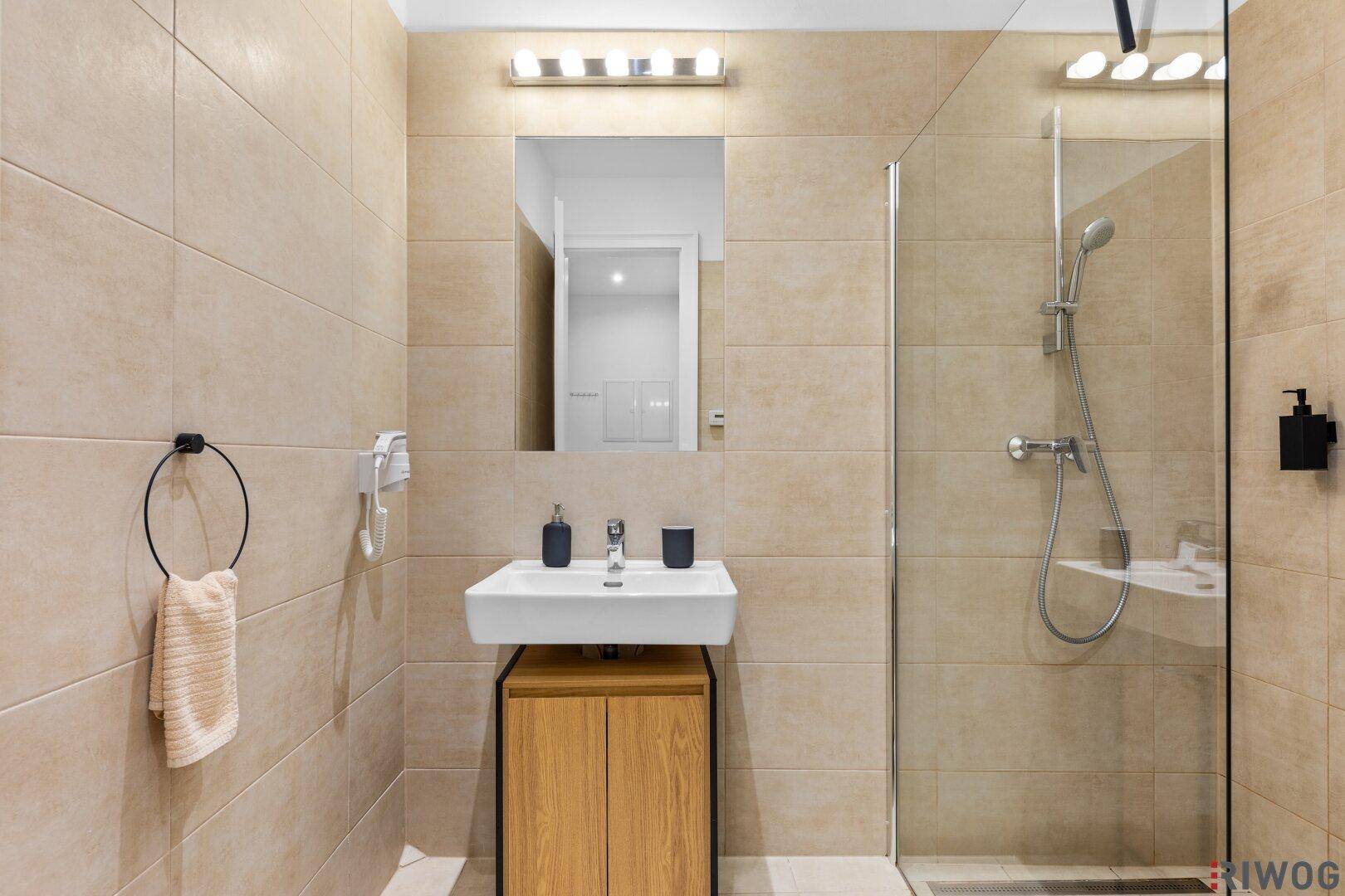 Modernes Badezimmer mit begehbarer Dusche, Einzelwaschbecken und hellen beigen Fliesen an den Wänden.