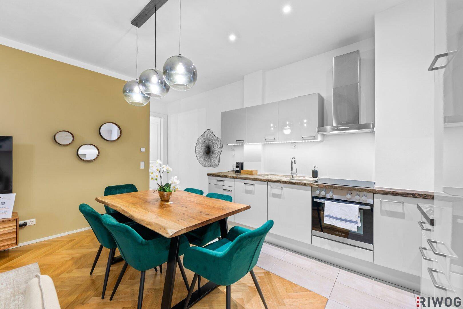 Moderne Einbauküche mit hellem Design, integriertem Backofen und Essbereich mit rustikalem Holztisch.