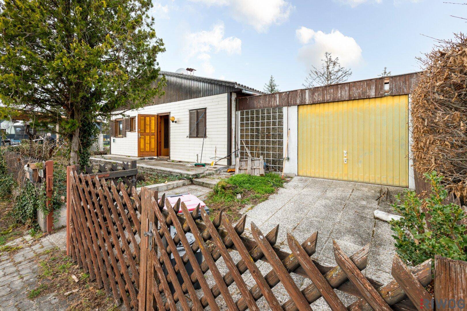 Außenansicht des Hauses mit Garage und Zufahrt, umgeben von einem Holzzaun.