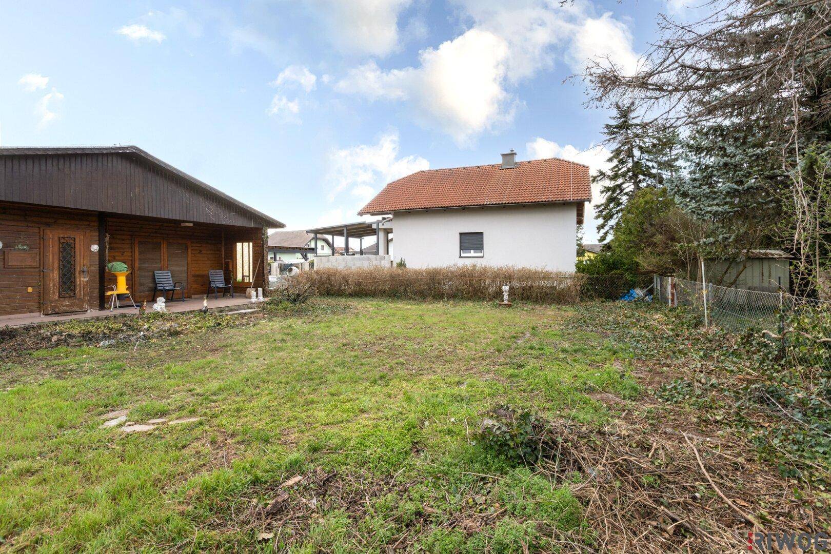 Gartenansicht mit dem Haus und angrenzenden Nachbargrundstücken unter blauem Himmel.