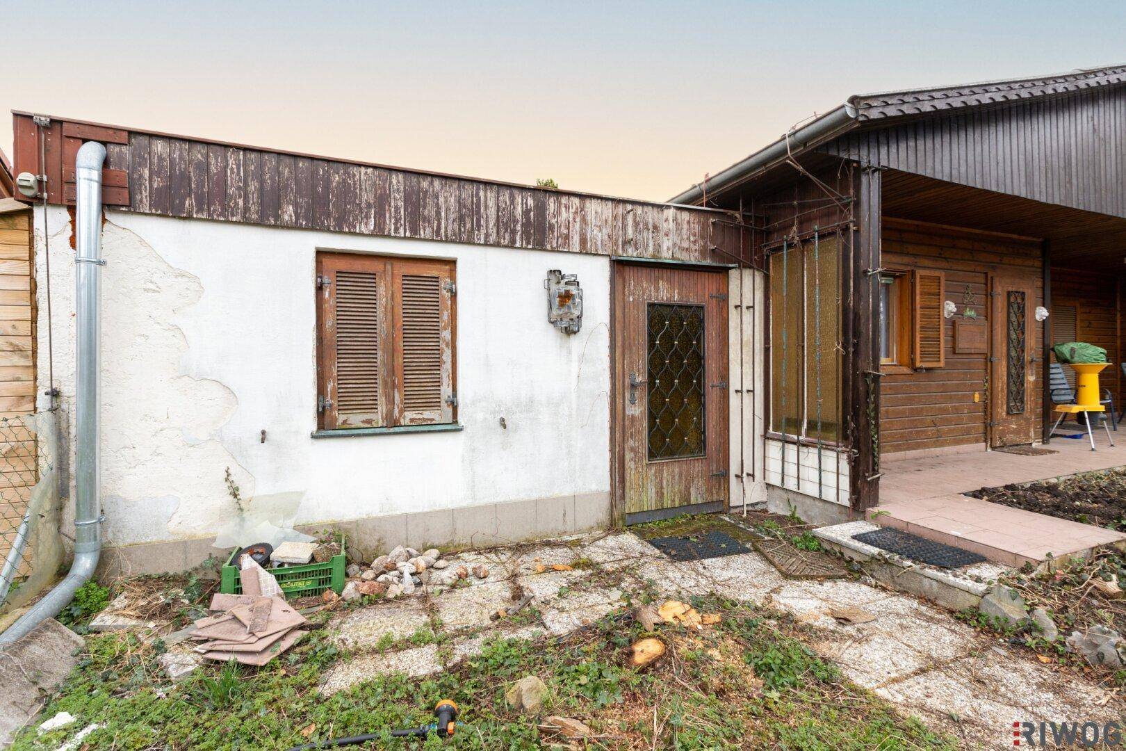 Seitenansicht des Hauses mit weißer Fassade, Holztür und angrenzendem Anbau.