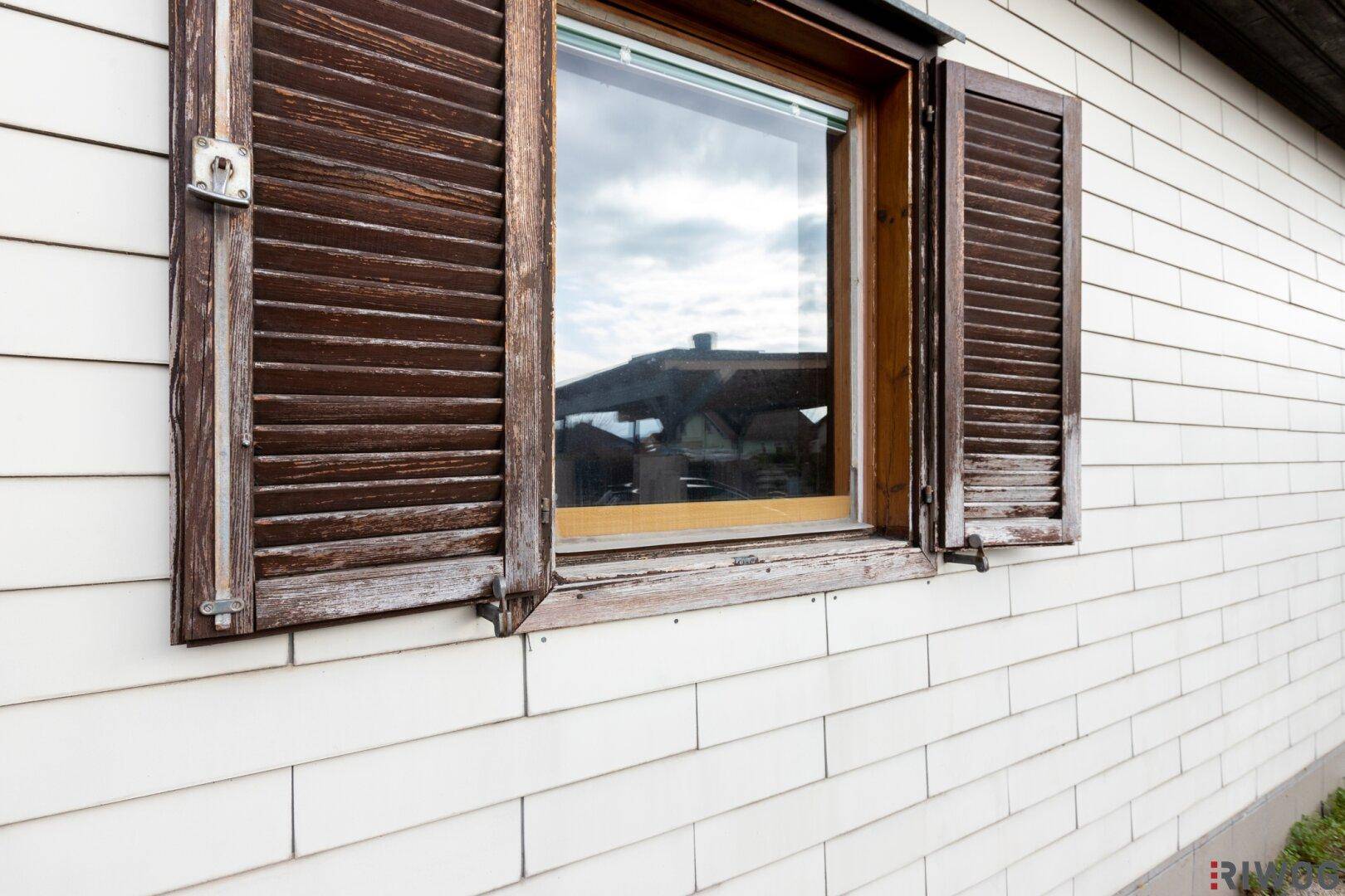 Nahaufnahme eines Holzfensters mit braunen Fensterläden an der weißen Hausfassade.