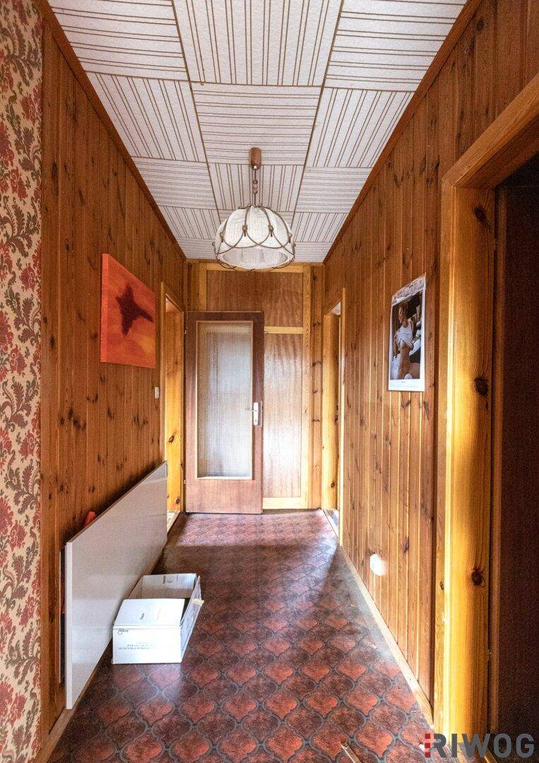Langer Flur mit Holzvertäfelung, gemustertem Boden und Deckenpaneelen im Vintage-Stil.