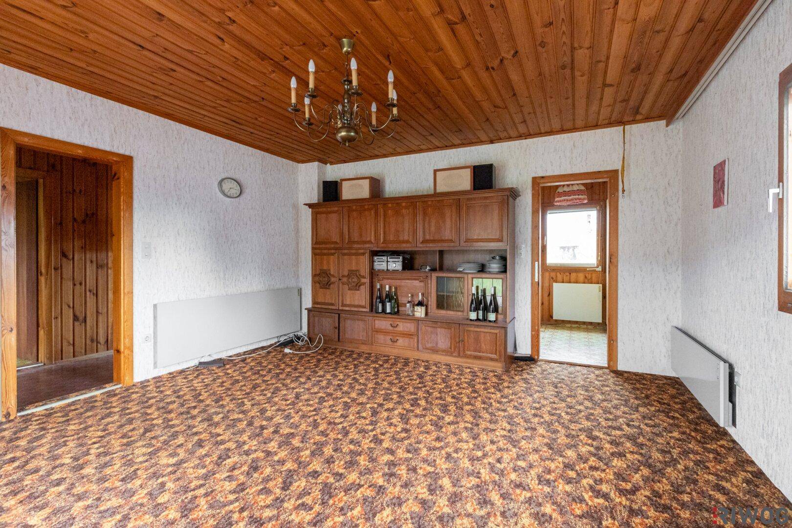 Wohnzimmer mit Holzdecke, Teppichboden und einem großen Holzschrank im traditionellen Stil.