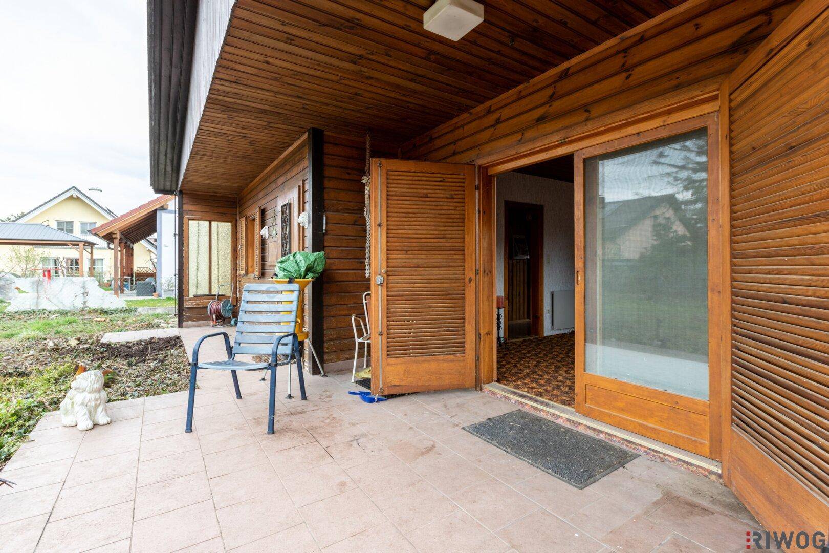 Überdachte Terrasse mit Fliesenboden und Sitzgelegenheiten, direkt vom Wohnzimmer zugänglich.