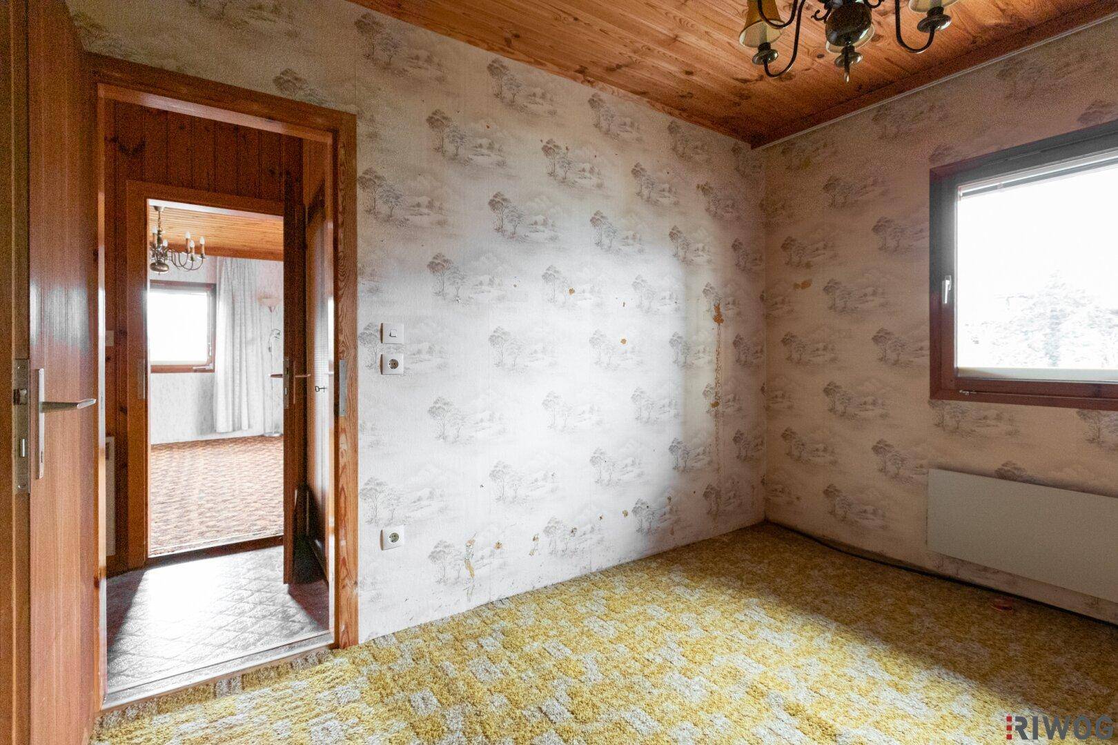 Schlafzimmer mit Holzdecke, Teppichboden und Zugang zu einem weiteren Raum.