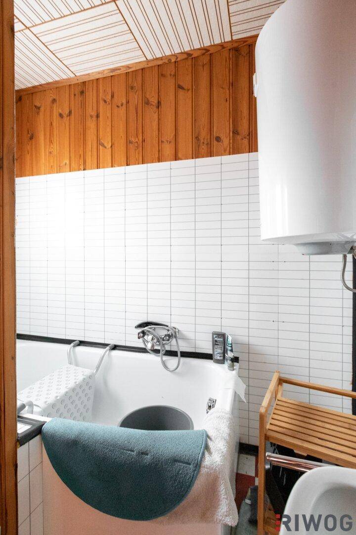 Nahaufnahme der Badewanne in einem Badezimmer mit weißen Fliesen und Holzvertäfelung.