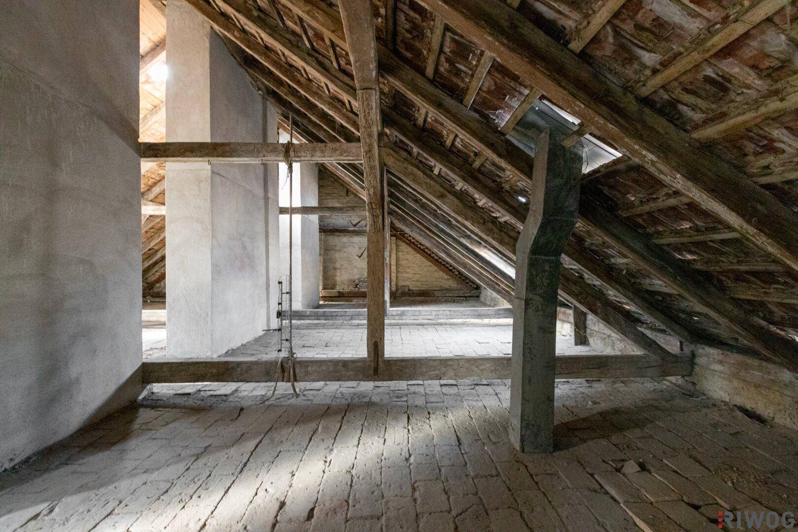 Langer Dachbodenbereich mit sichtbaren Holzbalken und Ziegelboden, bietet viel Potenzial.