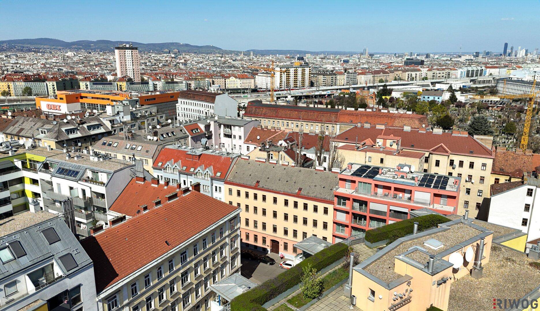 Panoramablick über die Stadt mit vielfältiger Architektur und grünen Dächern unter blauem Himmel.