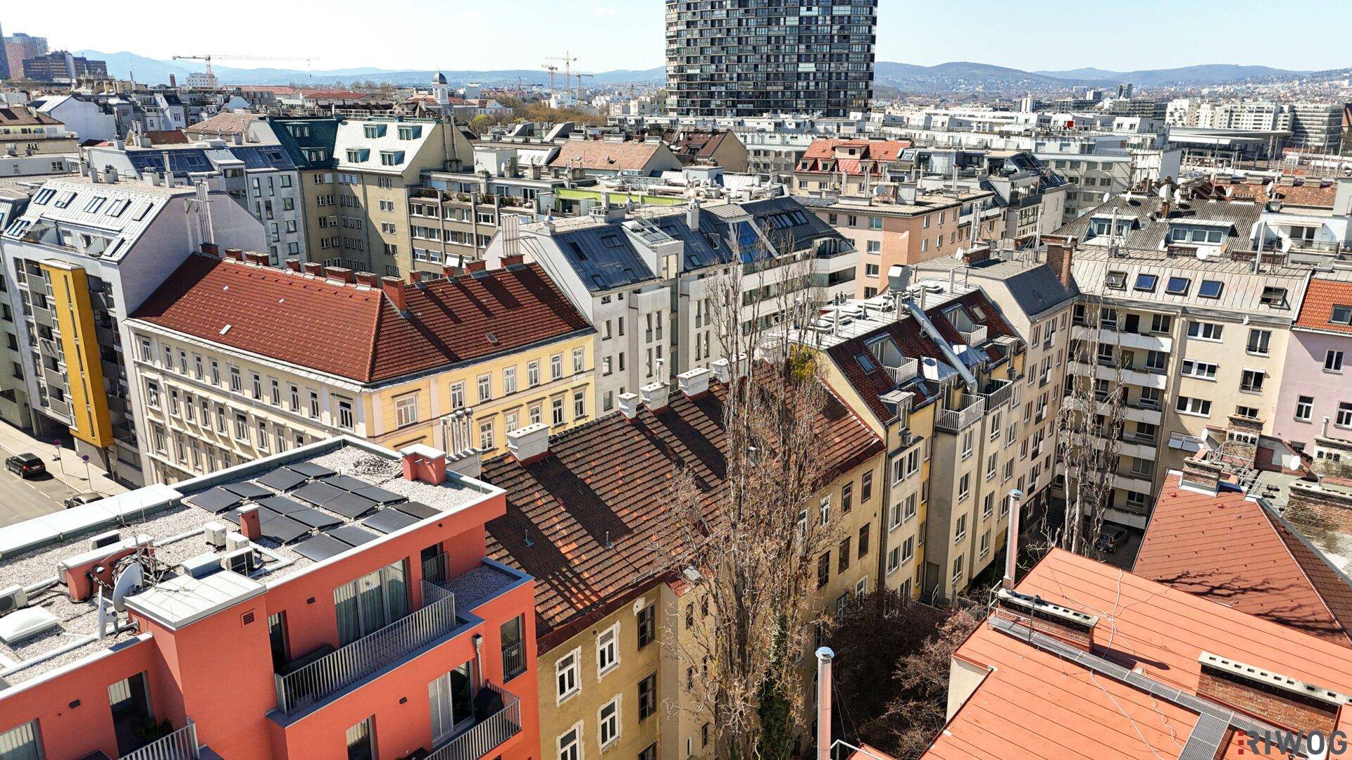Luftaufnahme eines Wohnviertels mit verschiedenen Gebäuden und Dächern unter blauem Himmel.