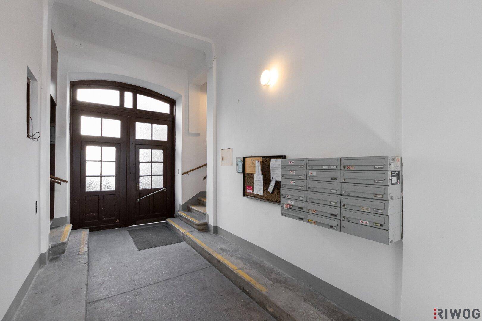 Heller Eingangsbereich eines Mehrfamilienhauses mit Briefkästen, einer Rampe und einer Holztreppe.